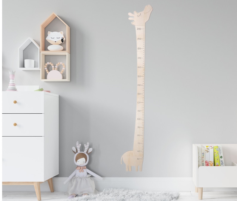 May include: Wooden giraffe height chart with a light brown finish. The chart features a giraffe silhouette with a measuring scale from 50 to 200 centimeters. The chart is mounted on a light gray wall in a nursery setting.