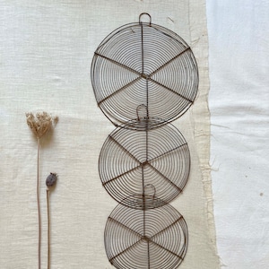May include: Three round, wire cooling racks stacked on top of each other. The racks are made of thin, brown wire and have a circular design. The racks are on a white linen background.