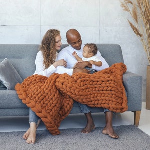 Happy family sitting on the couch with baby on the knees and getting cozy with ginger chunky knit blanket