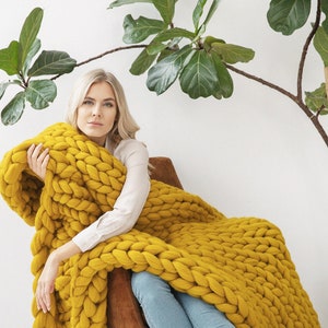 Lady is holding with her new Chunky knit blanket in Mustard