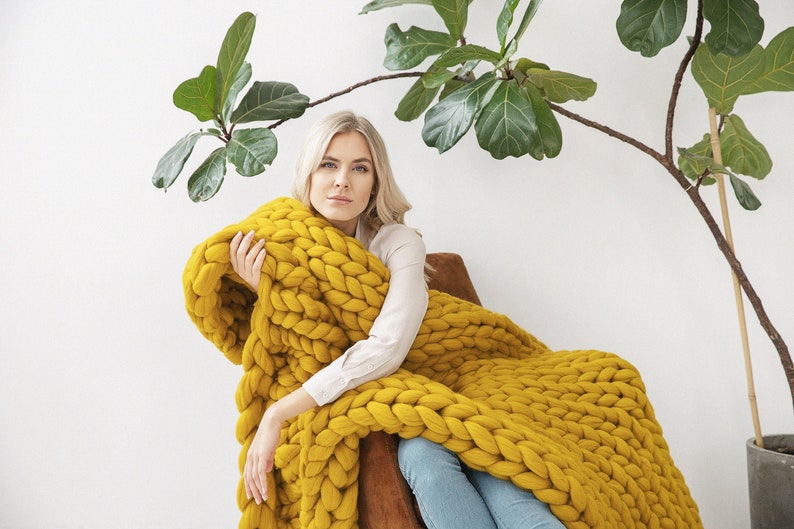 Lady is holding with her new Chunky knit blanket in Mustard