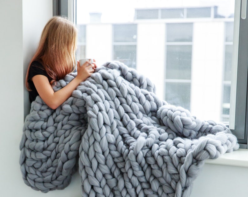 Lady sitting at the window with grey chunky knit blanket made from pure merino wool