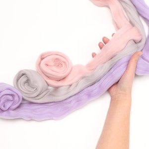 lady is holding merino wool roving in pink purple and grey