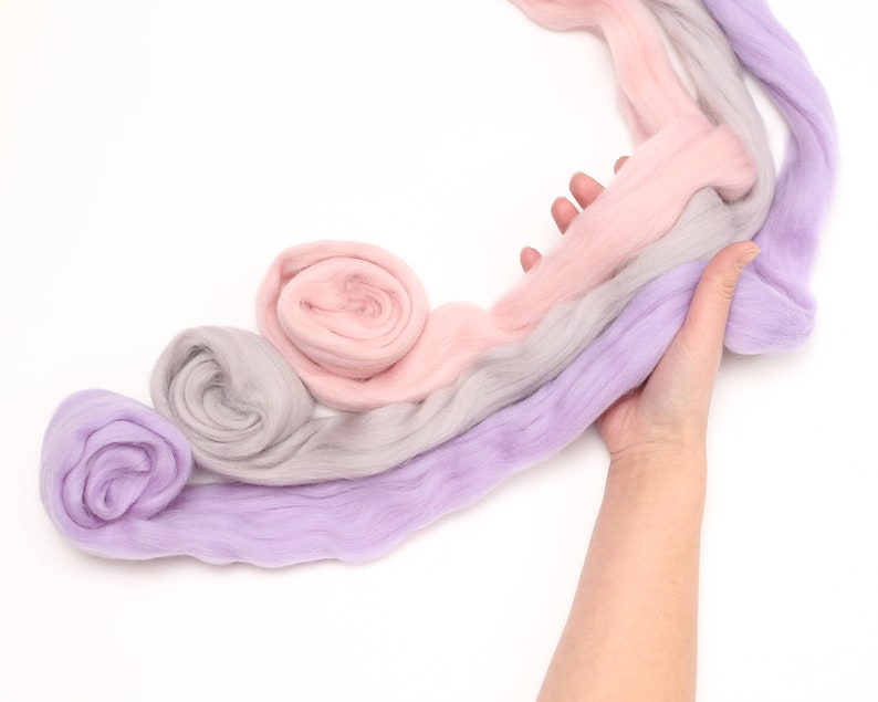 lady is holding merino wool roving in pink purple and grey