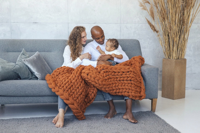 Happy family sitting on the couch with baby on the knees and getting cozy with ginger chunky knit blanket