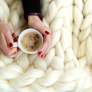 hands holding cup of hot coffee on top of the Merino wool blanket in white