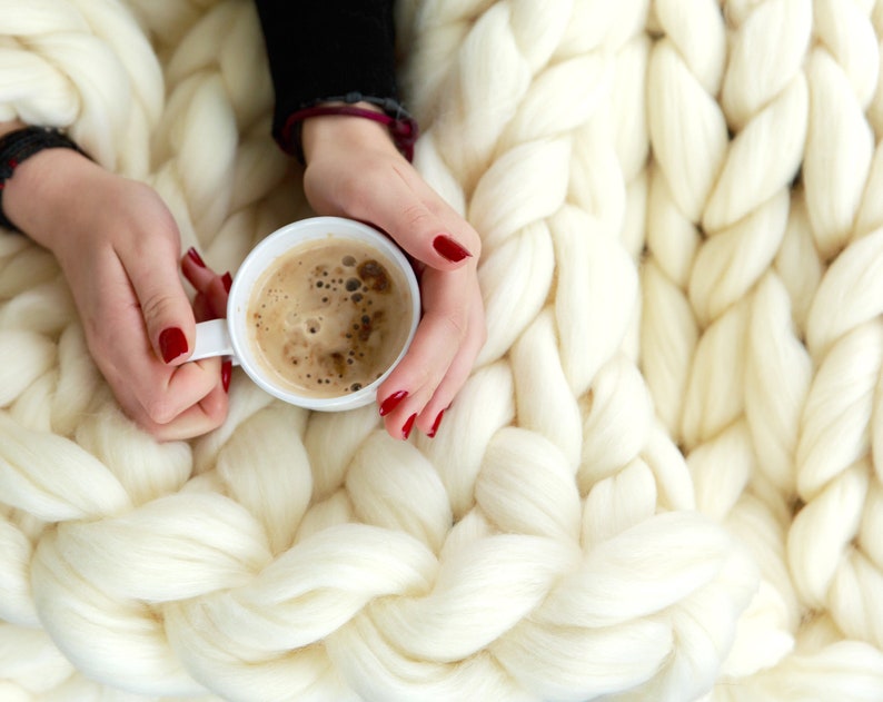 hands holding cup of hot coffee on top of the Merino wool blanket in white