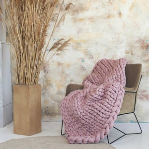 Dusty Pink chunky knit blanket on. chair in a cozy room