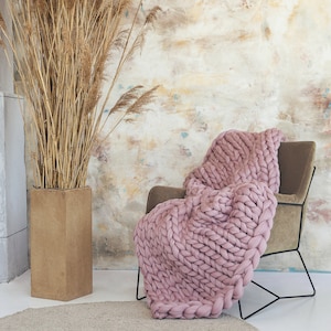 Dusty Pink chunky knit blanket on. chair in a cozy room