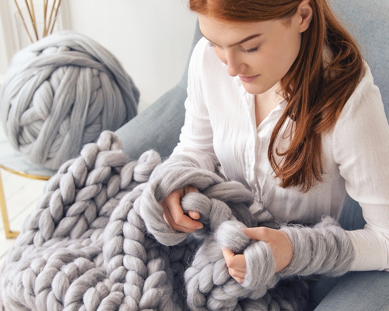 Lady extremely happy with her new hobby- chunky merino wool yarn that she is using to arm knitting a chunky blanket