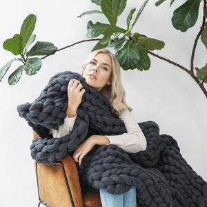 Lady holding a cozy and soft chunky knit blanket in dark grey