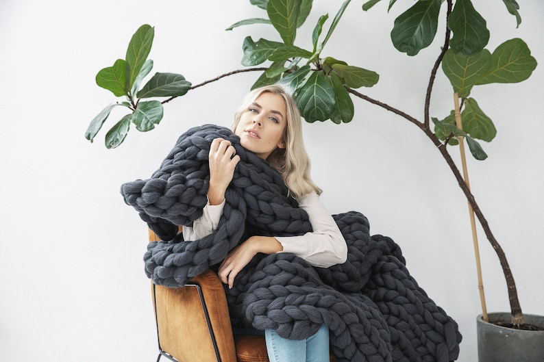 Lady holding a cozy and soft chunky knit blanket in dark grey