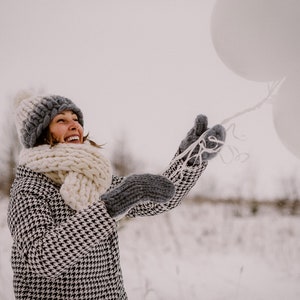 lady playing in winter outside wearing white chunky knit merino wool scarf mittens and pom pom hat