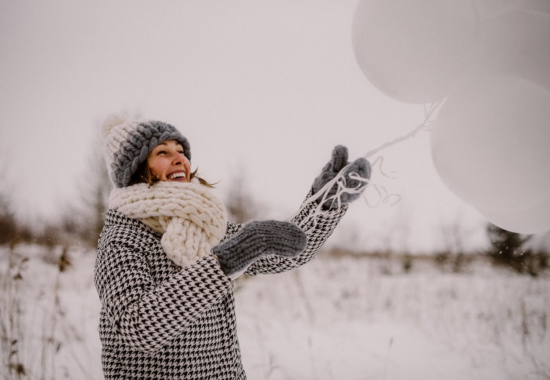 lady playing in winter outside wearing white chunky knit merino wool scarf mittens and pom pom hat