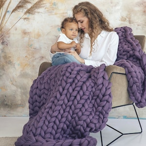 Lady with her baby sitting cozy with purple chunky blanket