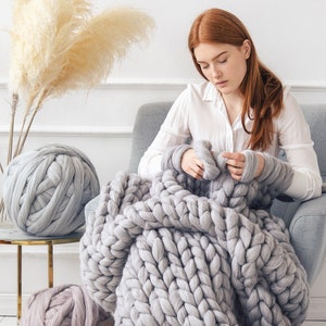 Lady knitting a grey chunky blanket at home