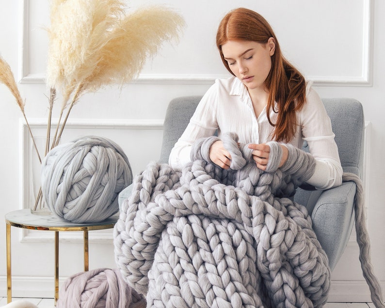 Lady knitting a grey chunky blanket at home