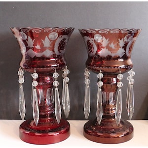 May include: Two ruby red glass candle holders with etched designs and crystal prism drops.