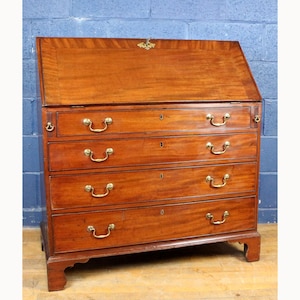 Puede incluir: Un escritorio secretario de caoba con una superficie de escritura inclinada y cuatro cajones. El escritorio presenta herrajes de latón, incluyendo tiradores y un cierre decorativo. La veta de la madera es visible.