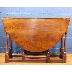 May include: A vintage wooden drop-leaf table with a semi-circular top. The table is made of a warm-toned wood, likely oak, and features turned legs and a decorative base. The table is approximately 122 cm wide when open.