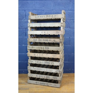 May include: A stack of eight wooden crates with various company names and dates printed on them. The crates are stacked on top of each other, with the oldest crate at the bottom and the newest crate at the top. The crates are all made of natural wood and have a rustic appearance.
