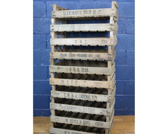 Puede incluir: Una pila de ocho cajas de madera con varios nombres de empresas y fechas impresos en ellas. Las cajas están apiladas una encima de la otra, con la caja más antigua en la parte inferior y la más nueva en la parte superior. Las cajas están todas hechas de madera natural y tienen un aspecto rústico.
