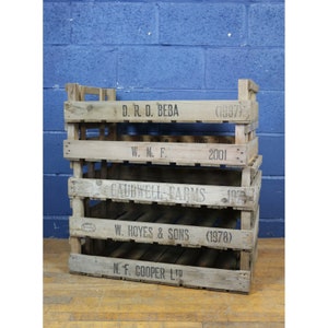 May include: A stack of four wooden crates with various labels and dates. The top crate reads "D. R. D. BEBA (1987)". The second crate reads "W. M. F. 2001". The third crate reads "CAUDWELL FARMS". The bottom crate reads "W. HOYES & SONS (1978)" and "N. F. COOPER LTD".