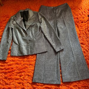 May include: A silver glitter suit set, including a blazer and wide-leg pants. The blazer has a notched collar and button closure. The pants have a high waist. The suit is displayed on an orange shag carpet.