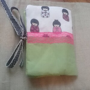 Copertina del libro tascabile in tessuto di cotone nelle tonalità del verde, rosa e bianco crema con stampe di bambole giapponesi.