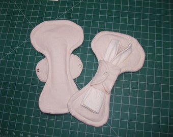 May include: Two white fabric pads with snaps. One pad is folded and the other is flat.