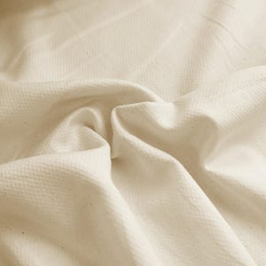 May include: Close-up of a textured, off-white fabric with a subtle woven pattern. The fabric is soft and drapes nicely.