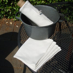 May include: A stack of five white cotton dish towels folded on a black metal table with a gray enamel pot in the background.