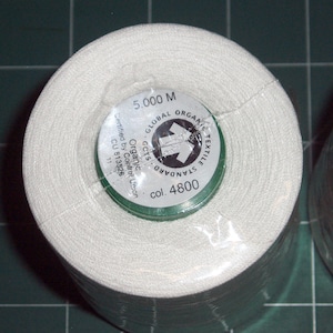 May include: A white spool of thread with a green label that reads "GLOBAL ORGANIC TEXTILE STANDARD GOTS Organic Certified by Control Union CU 813526 11 col. 4800 5,000 M".