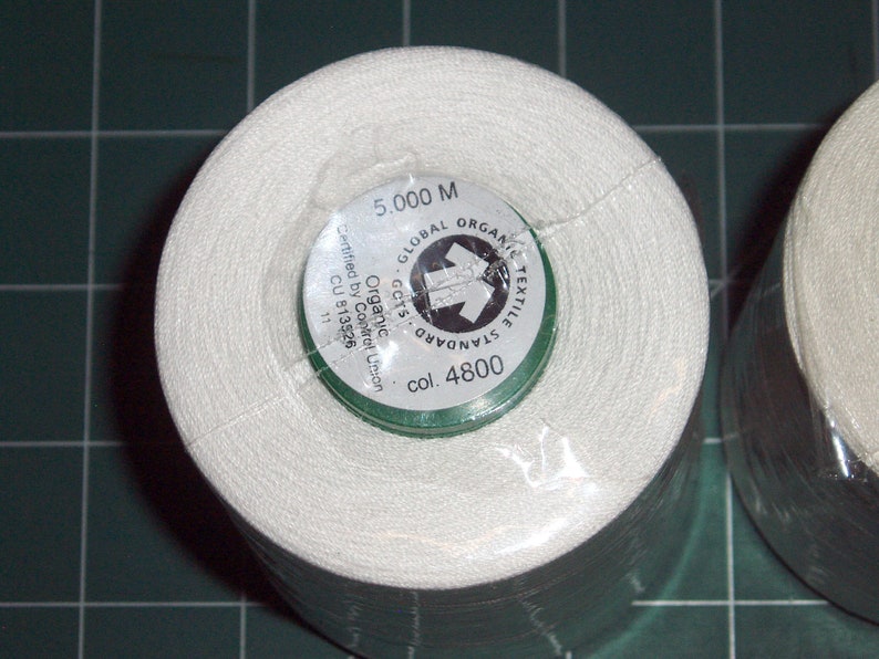 May include: A white spool of thread with a green label that reads "GLOBAL ORGANIC TEXTILE STANDARD GOTS Organic Certified by Control Union CU 813526 11 col. 4800 5,000 M".