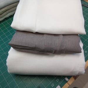 May include: Three pieces of fabric stacked on top of each other. The top piece is white, the middle piece is gray, and the bottom piece is white. The fabric is on a green cutting mat.