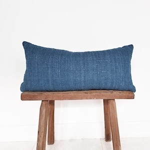 May include: A blue rectangular cushion sits on a wooden bench. The cushion is made of a textured fabric and has a simple, modern design.