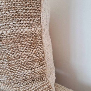 May include: Close-up of a beige woven throw pillow with a textured surface.