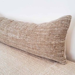 May include: A long, rectangular, beige throw pillow with a woven texture.