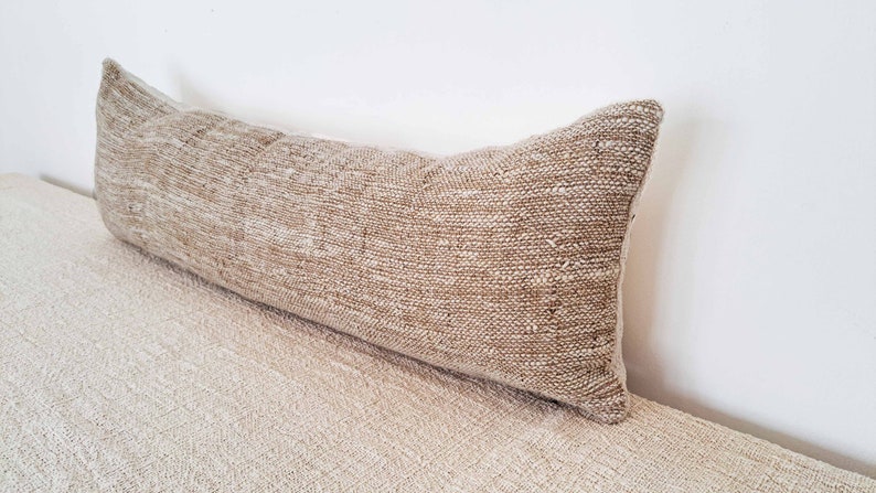 May include: A long, rectangular, beige throw pillow with a woven texture.