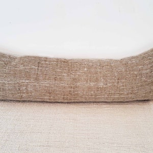 May include: A long, rectangular, brown and beige throw pillow with a woven texture.