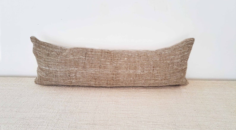 May include: A long, rectangular, brown and beige throw pillow with a woven texture.
