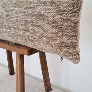 May include: A beige rectangular pillow with a zipper closure on a wooden stool. The pillow is made of a textured fabric with a subtle sheen.