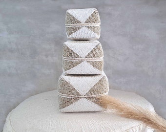 May include: Three stacked square boxes made of woven natural fibers with a geometric pattern in white and beige.