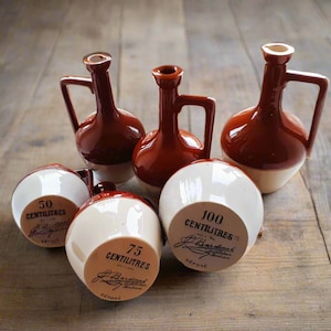 Può includere: Una collezione di brocche e bottiglie in ceramica nei toni del marrone e del bianco. Le brocche hanno manici e sono etichettate con misure in centilitri, da 50 a 100. Le bottiglie hanno un design classico.