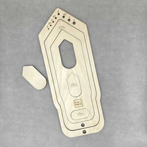 Könnte beinhalten: Ein Holzwerkzeug mit mehreren runden Ausschnitten und einem rechteckigen Ausschnitt mit dem Text "KAI NOR" in der Mitte. Das Werkzeug ist zum Basteln gedacht und hat ein kleines, separates Holzstück.