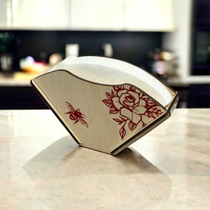 May include: A wooden coffee filter holder featuring a red rose and bee design. The holder is made of light wood and has a white filter inside.