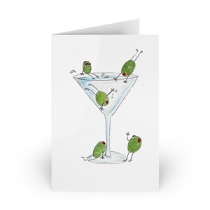 Può includere: Biglietto di auguri bianco con un'illustrazione umoristica di olive verdi in un bicchiere da Martini. Le olive hanno braccia e gambe, alcune con occhiali da sole, che si godono la bevanda. Il bicchiere da Martini è pieno di un liquido trasparente.