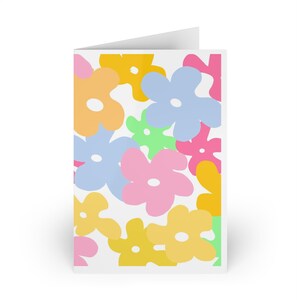 Puede incluir: Una tarjeta de felicitación plegada con un fondo blanco y un patrón repetido de grandes flores coloridas. Las flores son en tonos de amarillo, naranja, rosa, azul y verde. La tarjeta está en blanco por dentro.