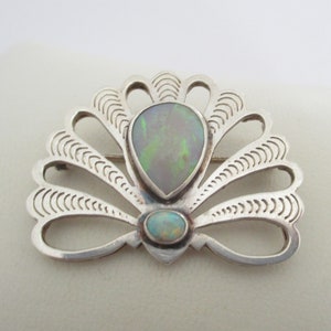 May include: A silver brooch with a fan-shaped design and two opal stones. The brooch is made of sterling silver and features a delicate, intricate design.