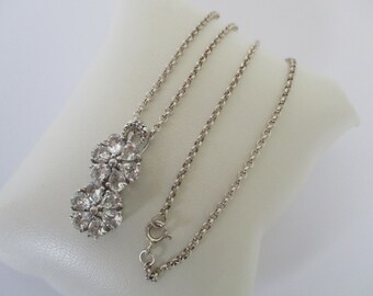 May include: A silver chain necklace with a pendant featuring two clusters of clear cubic zirconia stones in a flower shape.